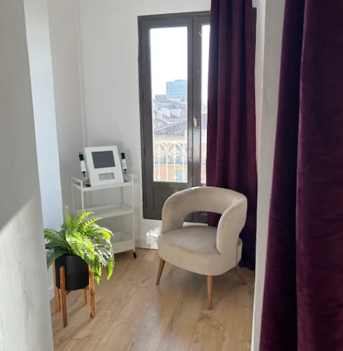 Une belle salle lumineuse avec parquet, fauteuil en velours, rideaux prunes et la machine MILTA/Dermapen sur desserte.